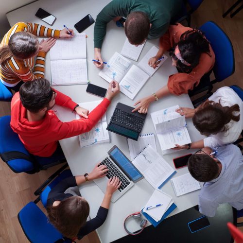 Top view of university students sitting at a table studying and working on laptop